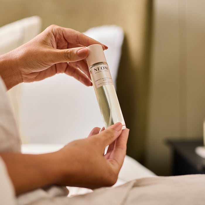 A person holding NEOM perfect night's sleep mist in a bedroom